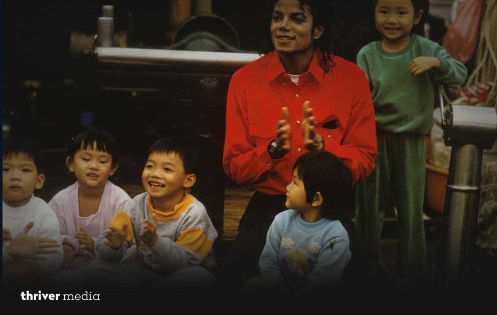 Michael Jackson sitting with a group of young children, clapping and smiling during a casual indoor gathering.