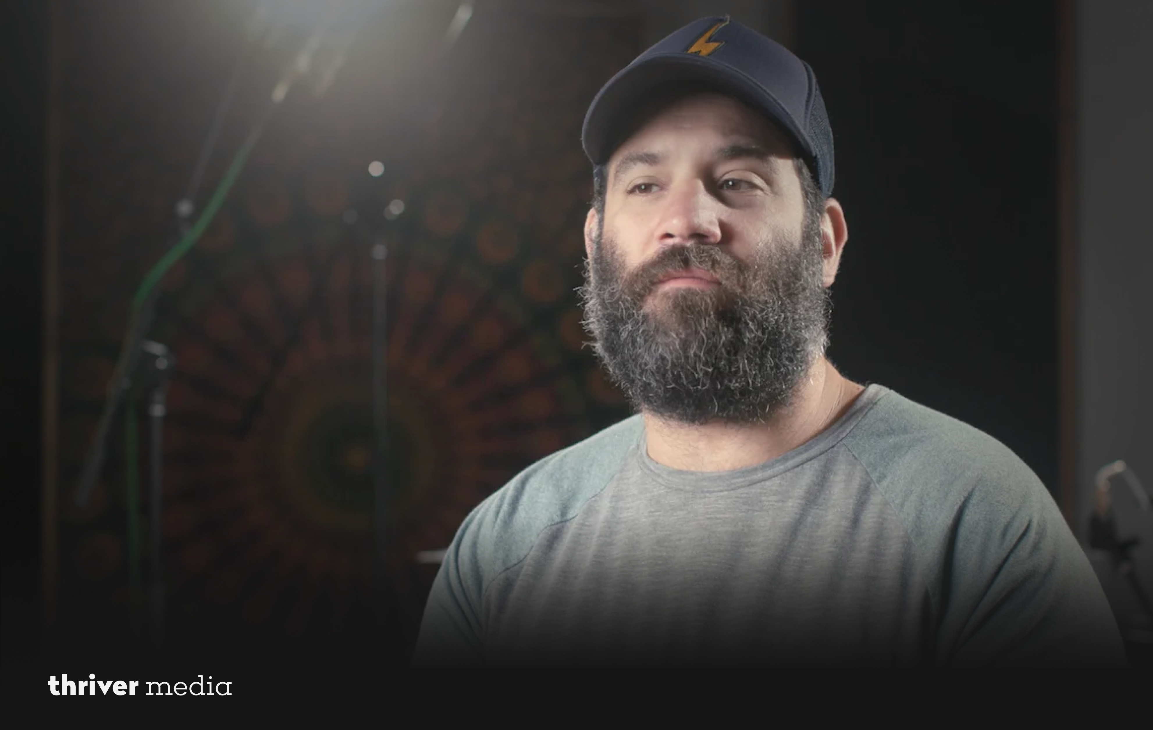 Portrait of Timothy Very wearing a cap and grey shirt, softly lit against a dark studio background.