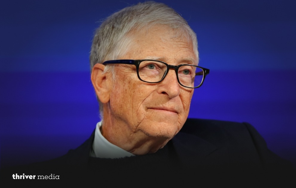 Close-up portrait of Bill Gates wearing glasses and a dark suit against a blue background.