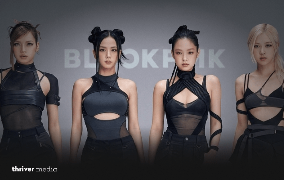 BLACKPINK members pose in coordinated black outfits against a minimalist backdrop with the group’s name behind them.