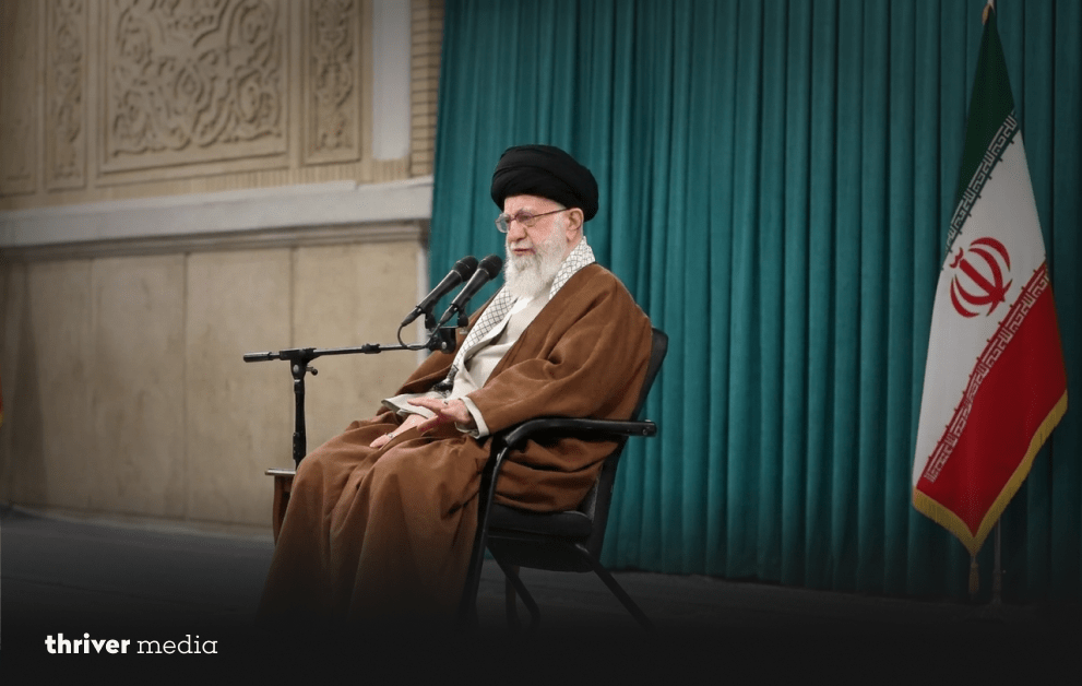 Ayatollah Ali Khamenei (1939-2026): History Bows Its Head 2 Ayatollah Ali Khamenei seated on a chair speaking into microphones, wearing traditional clerical robes, with green curtains and the Iranian flag in the background.
