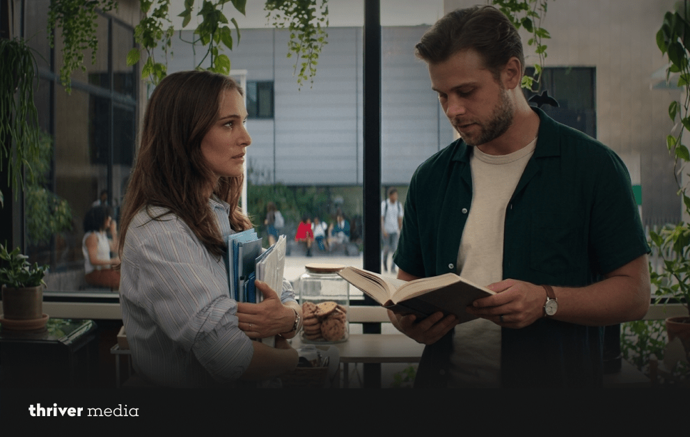 Two characters reading and discussing a book inside a plant-filled greenhouse in a scene from Vladimir.