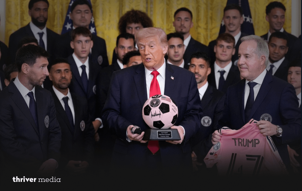 Donald Trump holds a signed soccer ball during a White House ceremony with Lionel Messi and Inter Miami players standing behind him.