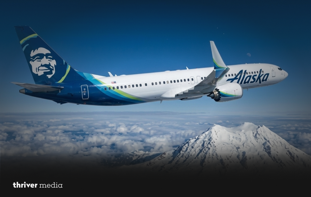 Alaska Airlines International Business Class Suite interior on Boeing 787-9 Dreamliner showing lie-flat seat in bed position, sliding privacy door, 17-inch entertainment screen, and Filson-branded amenity kit on side console.